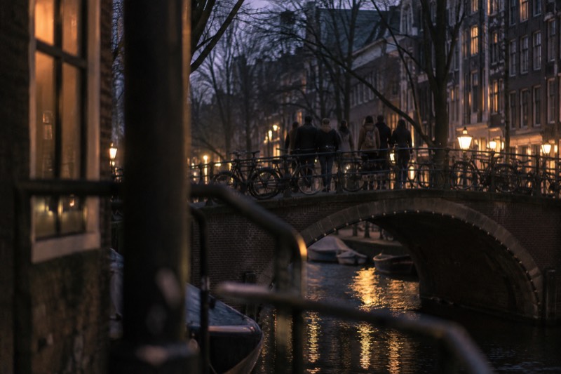 A walking group crossing a humpbacked bridge over a canal in the city centre, bicycles chained along both railings, Amsterdam, Netherlands