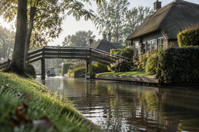 A wooden footbridge arching over a narrow canal between thatched cottages and clipped green gardens, Giethoorn, Netherlands