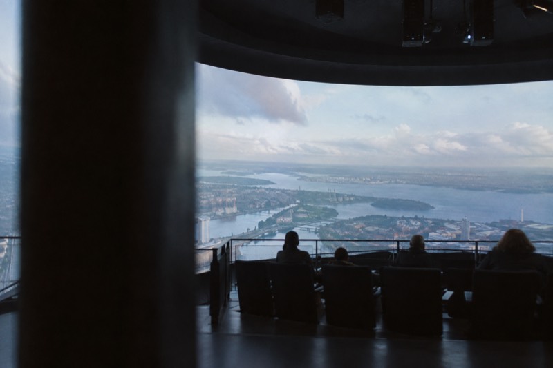 A darkened theatre with rows of seats suspended in front of an enormous curved screen filled with soft blue aerial light, Amsterdam Noord, Netherlands