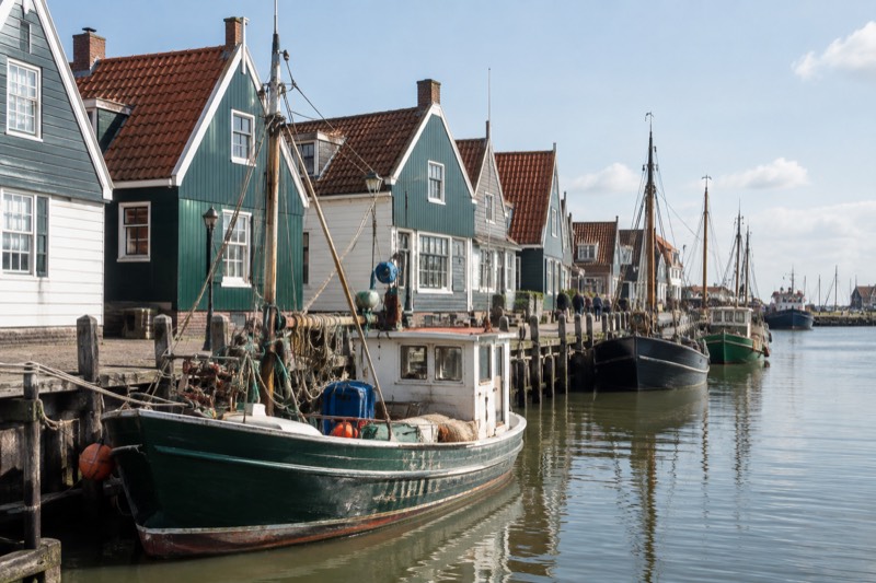 A harbour front of green and white wooden houses with fishing boats moored along the quay, Volendam, Netherlands