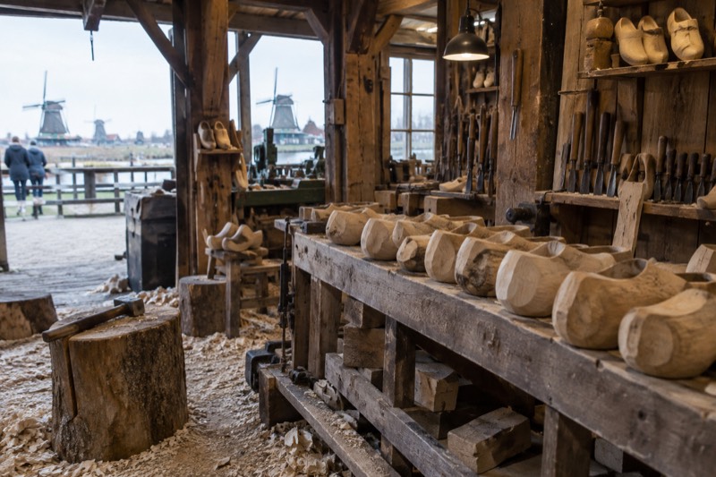 Rows of unpainted wooden clogs on a workbench in a timber workshop with wood shavings across the floor, Zaanse Schans, Netherlands