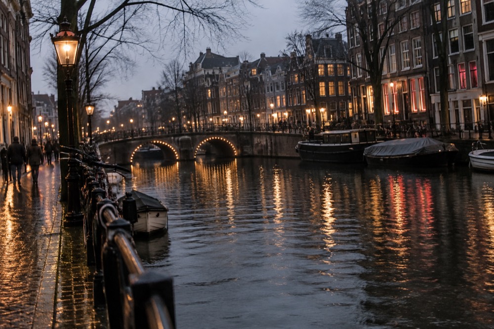 An Amsterdam canal at dusk with bridges and lit windows reflecting in the water
