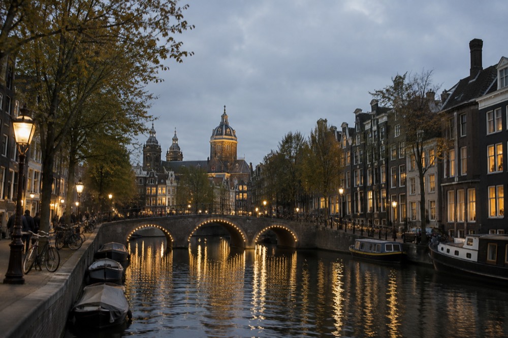 An Amsterdam canal at dusk with lit bridges and reflected window lights