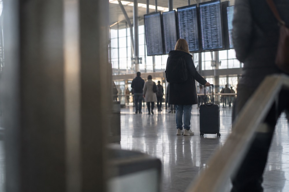 Traveller with a cabin bag checking a large flight information display in an airport concourse