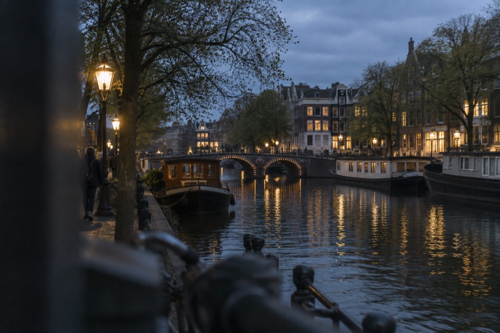 A wide canal in Amsterdam with houseboats and arched bridges in soft evening light