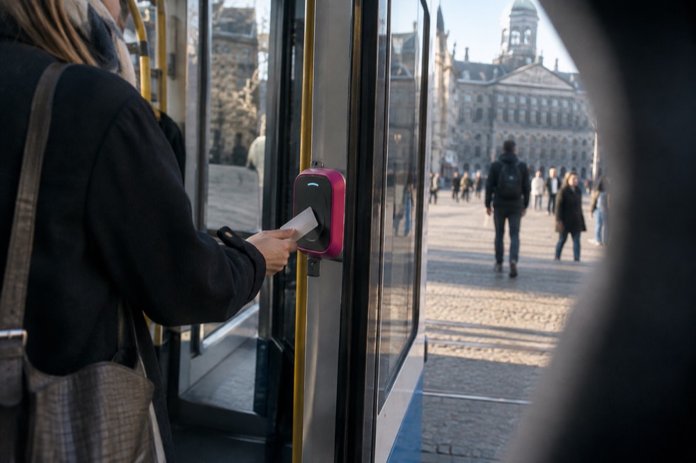 A contactless bank card tapped against a pink card reader beside tram doors