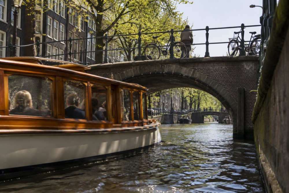 A classic saloon boat passing under a narrow canal bridge in the city centre
