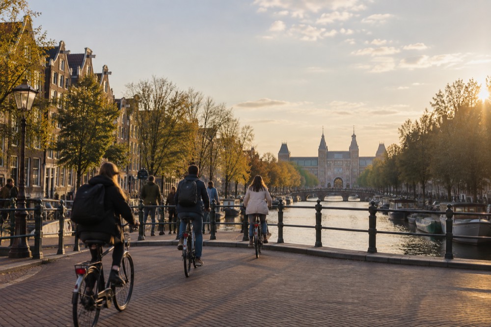 Cyclists crossing a bridge over a tree-lined canal toward Museumplein