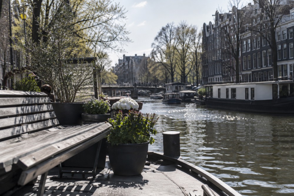 A houseboat deck with a bench and planters overlooking an Amsterdam canal in morning light