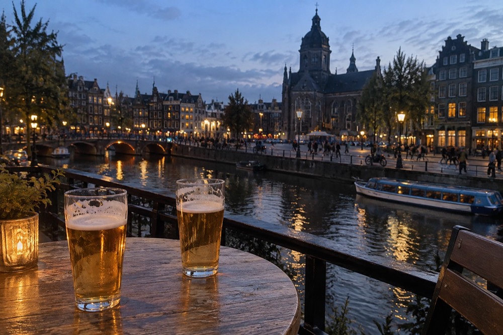 Two glasses of beer on a wooden café table beside an Amsterdam canal at dusk