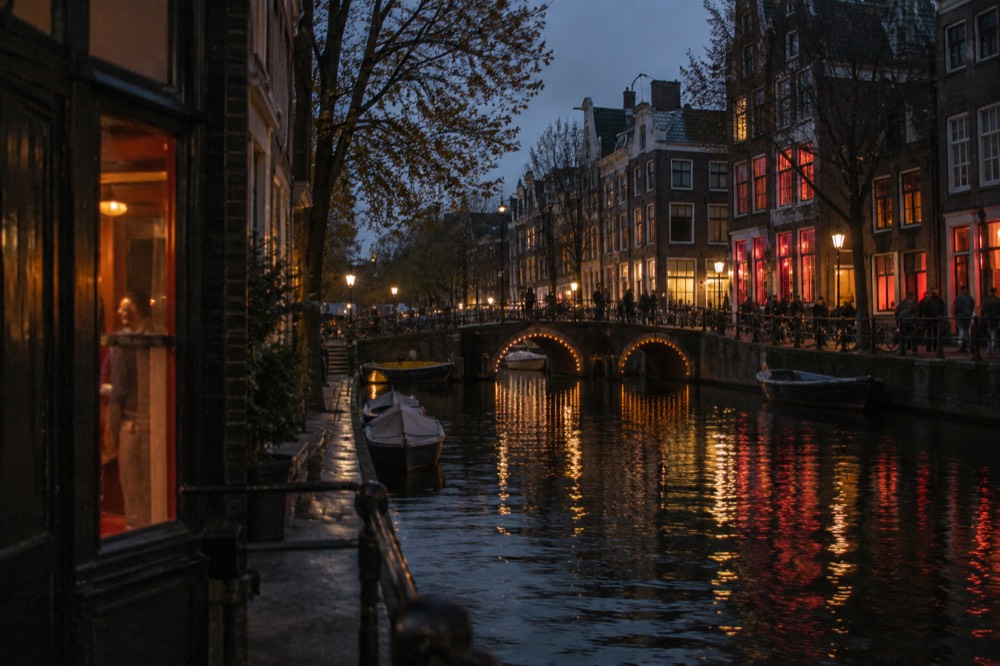 Old Amsterdam canal at night with warm window lights reflecting on dark water and narrow arched bridges