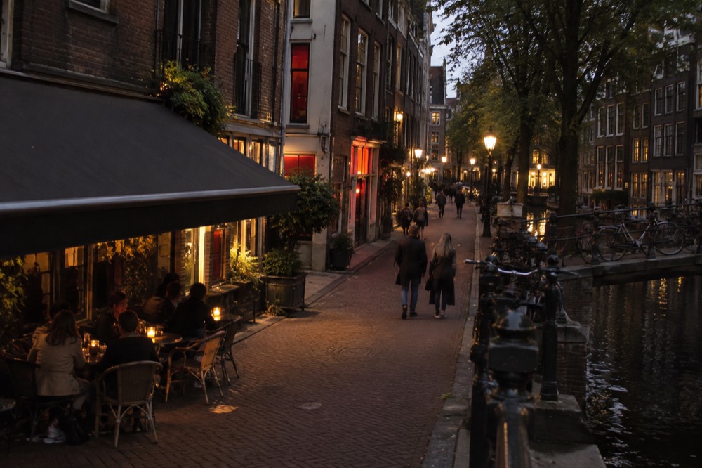 Narrow Amsterdam street in the old centre with traditional gabled brick buildings and a cafe terrace in daylight