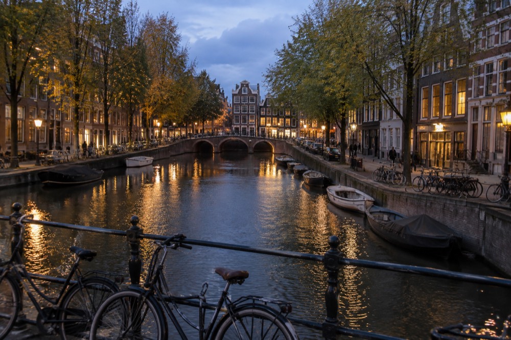 A canal in Amsterdam lined with narrow gabled houses and trees, seen from a small bridge