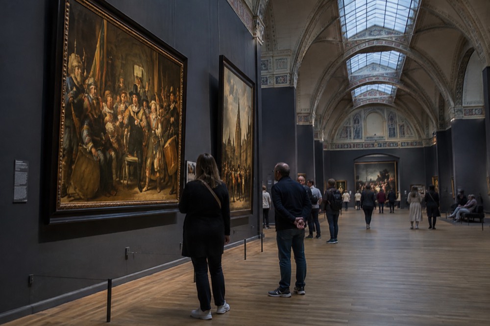 Gallery hall with visitors viewing large golden-age paintings in the Rijksmuseum
