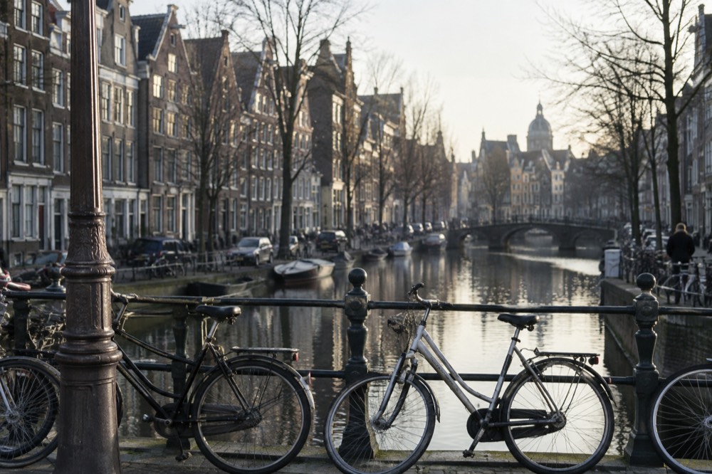 Gabled canal houses lining a quiet Amsterdam gracht with bicycles parked against a bridge railing