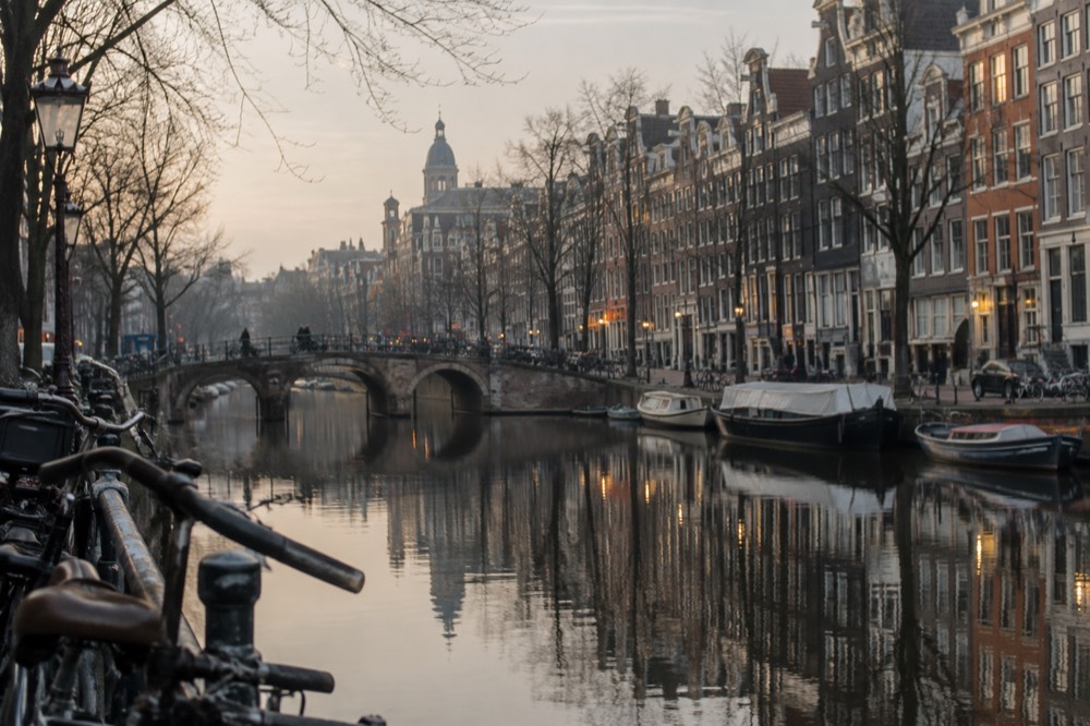 Amsterdam canal houses and bridge reflected in still water at dusk