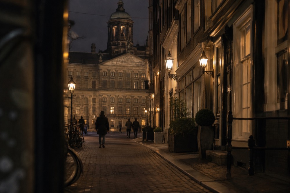 Narrow Amsterdam street lit by warm lamps on a quiet evening
