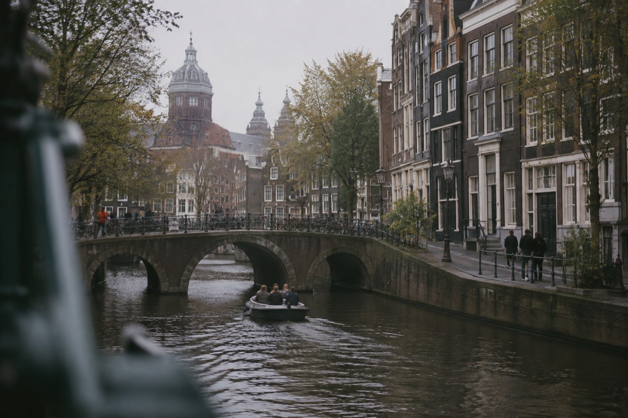 A canal in Amsterdam lined with narrow gabled houses and a small boat passing under a stone bridge
