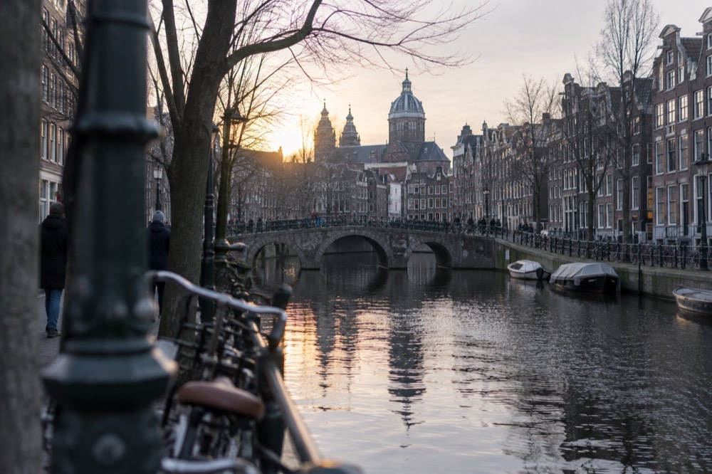An Amsterdam canal at dusk with bridges and narrow brick houses
