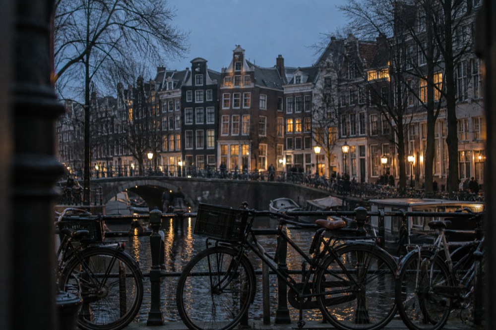 A row of bicycles parked on a canal bridge with gabled houses behind them