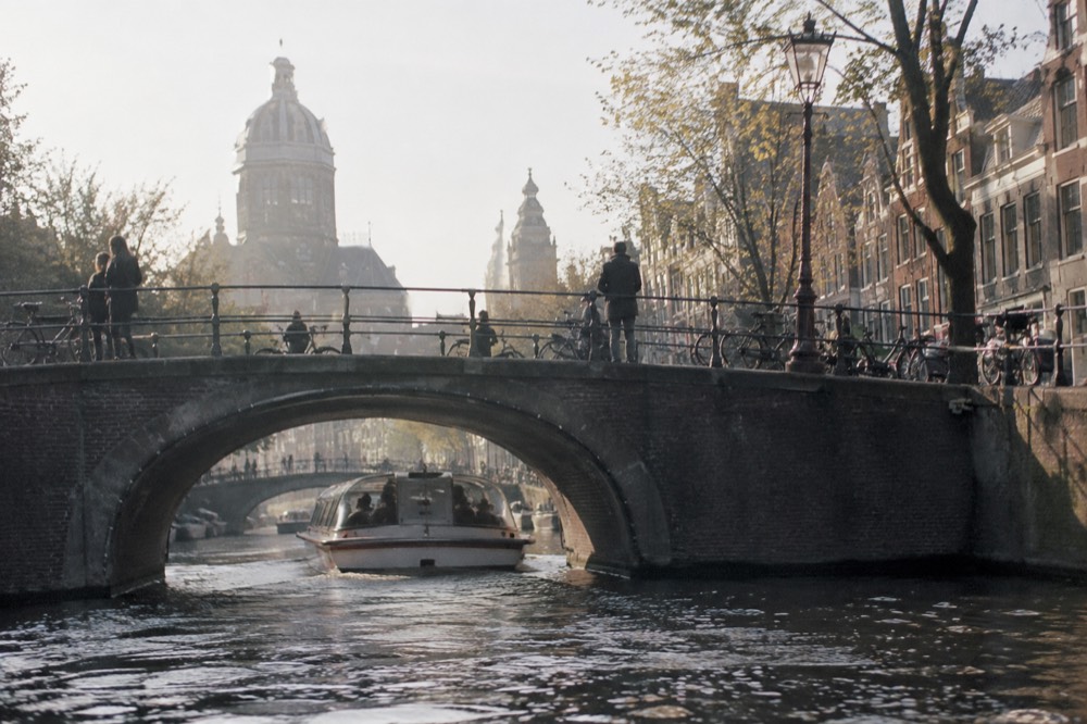 A canal boat passing under a stone bridge in the late afternoon light