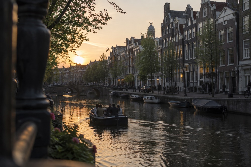 A small open canal boat passing gabled canal houses at dusk