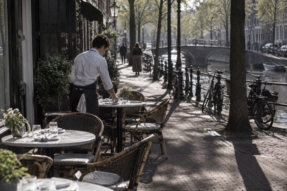 A waiter setting outdoor cafe tables on a quiet canal side street in the morning