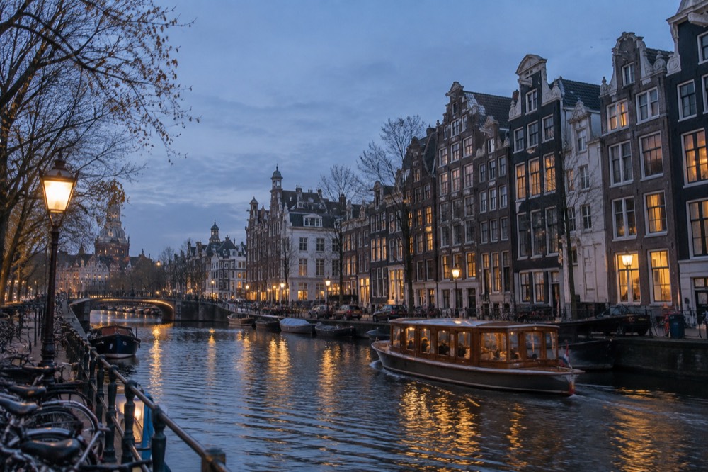A wooden saloon boat passing tall narrow gabled canal houses along a quiet Amsterdam canal
