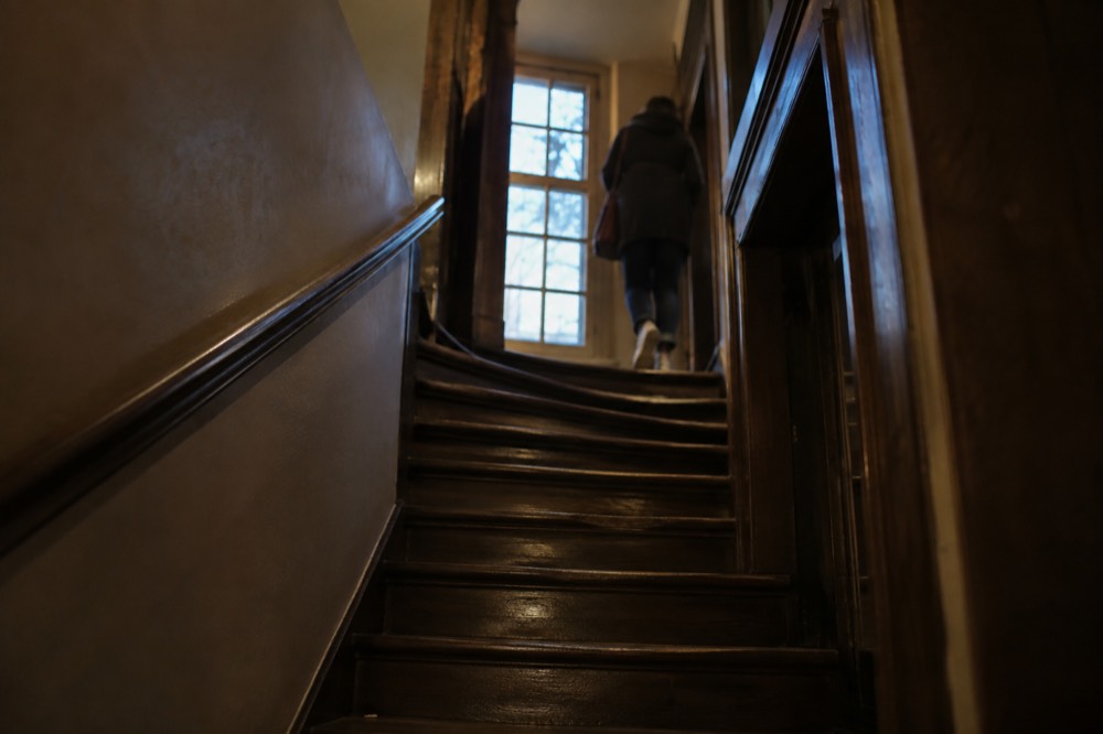 A narrow historic Amsterdam staircase lit by a window in an old canal house
