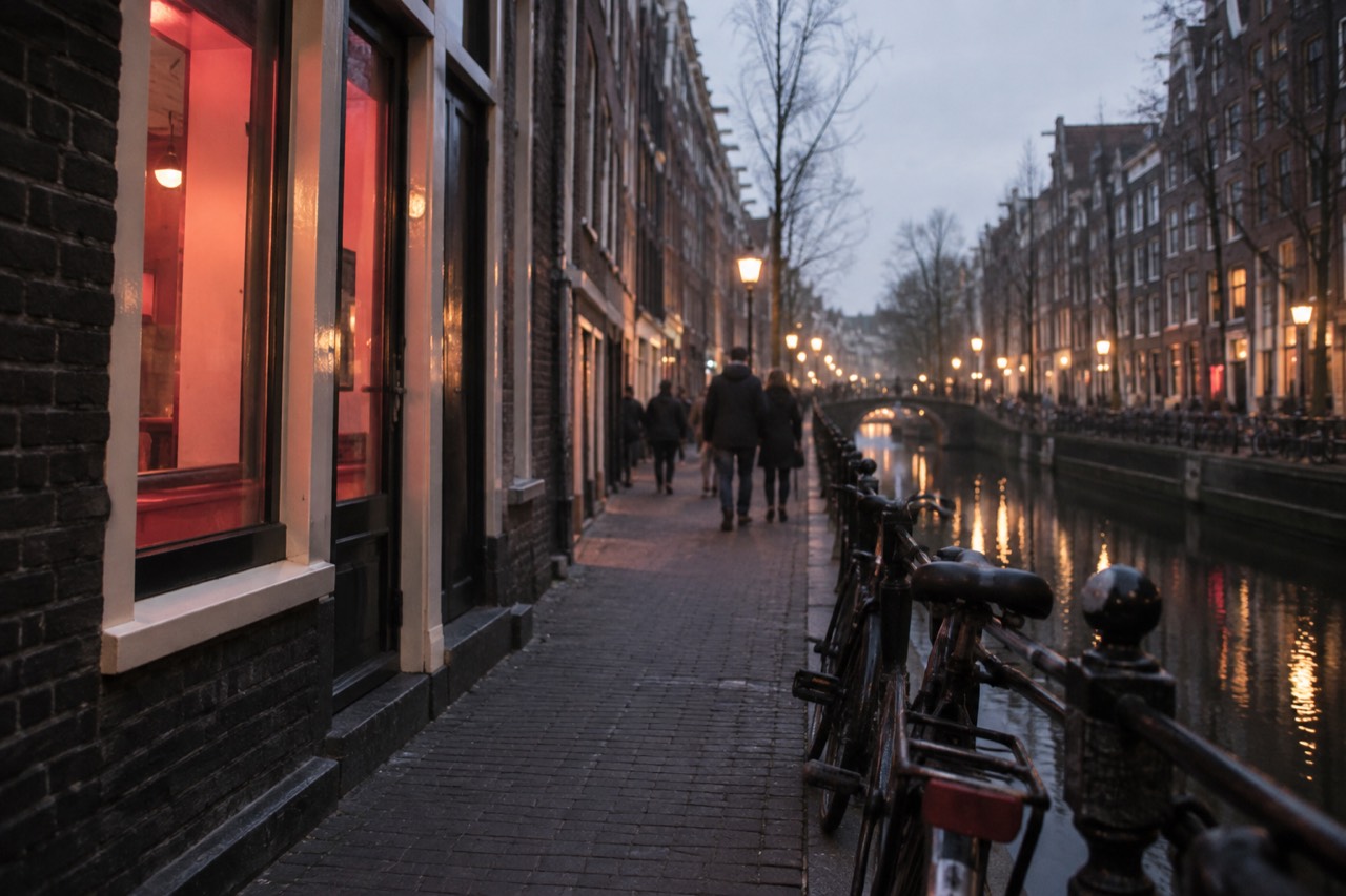 Narrow Amsterdam canal street at dusk with old brick buildings and warm window light