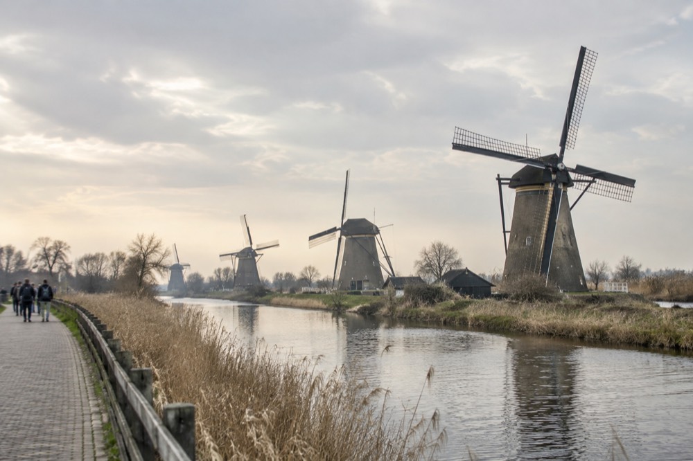 A row of historic windmills standing beside a drainage canal under a wide sky