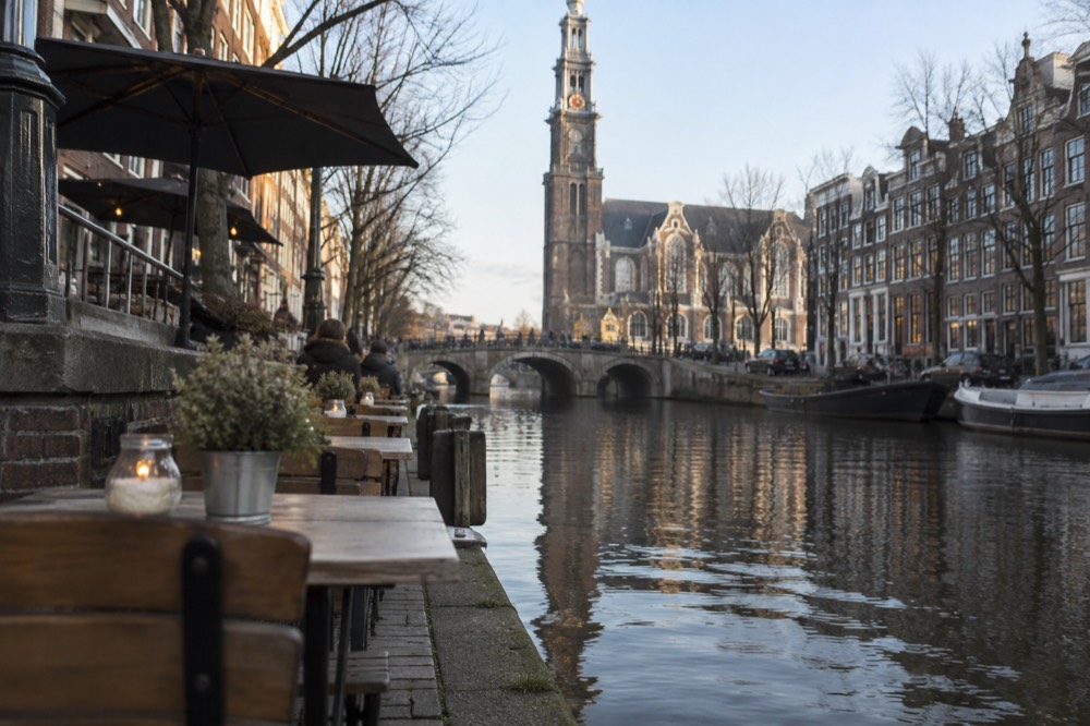 A canal with waterside cafe terraces on a lower level beside a tall church tower