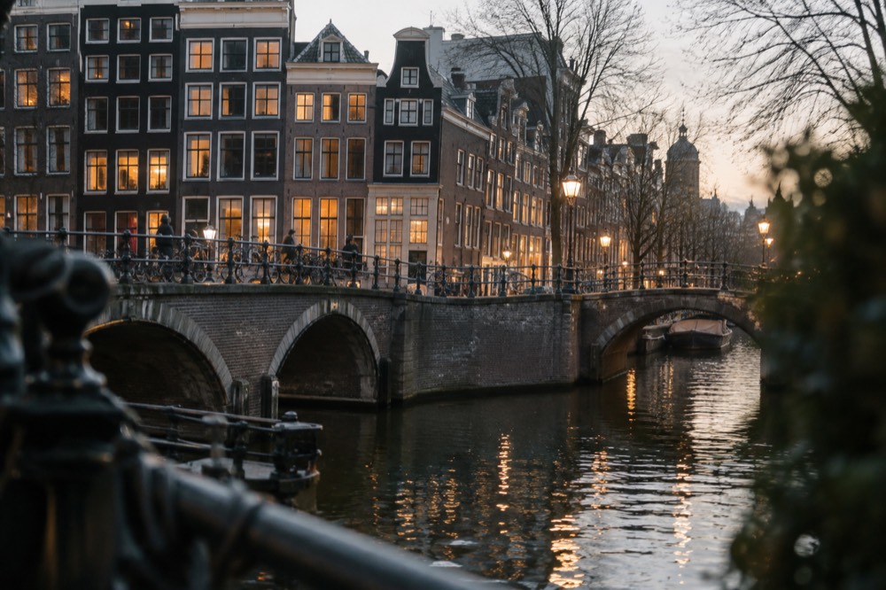 An Amsterdam canal bridge in the evening with lit houses reflected in the water