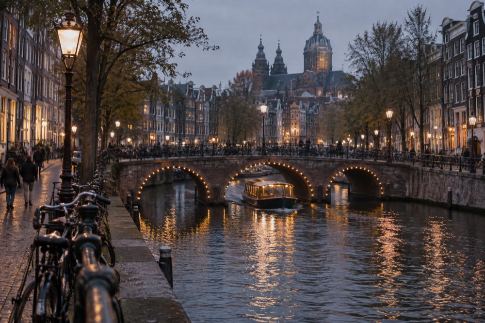 A small illuminated boat passing under a lit canal bridge at night
