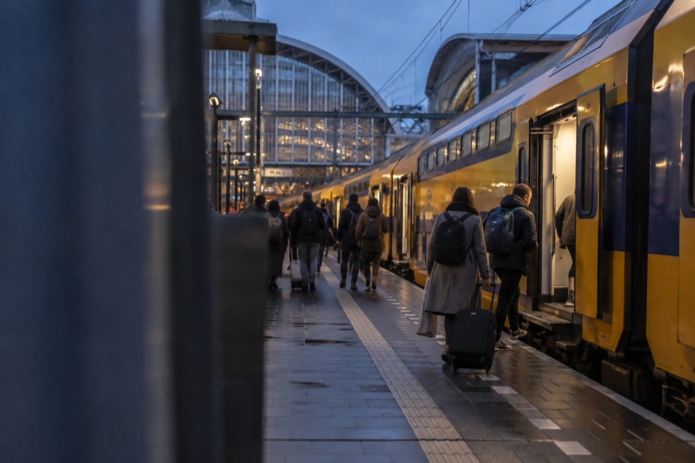 Amsterdam Centraal station platforms with a yellow double-decker train and passengers boarding.