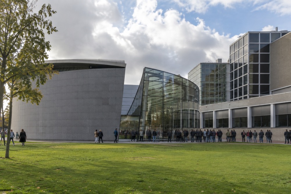 The Van Gogh Museum facade on Museumplein with visitors queuing beneath a large banner of a sunflower painting.