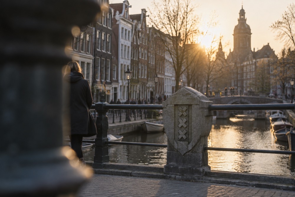 Historic Amsterdam street with canal houses and a stone shield bearing three crosses on a bridge railing