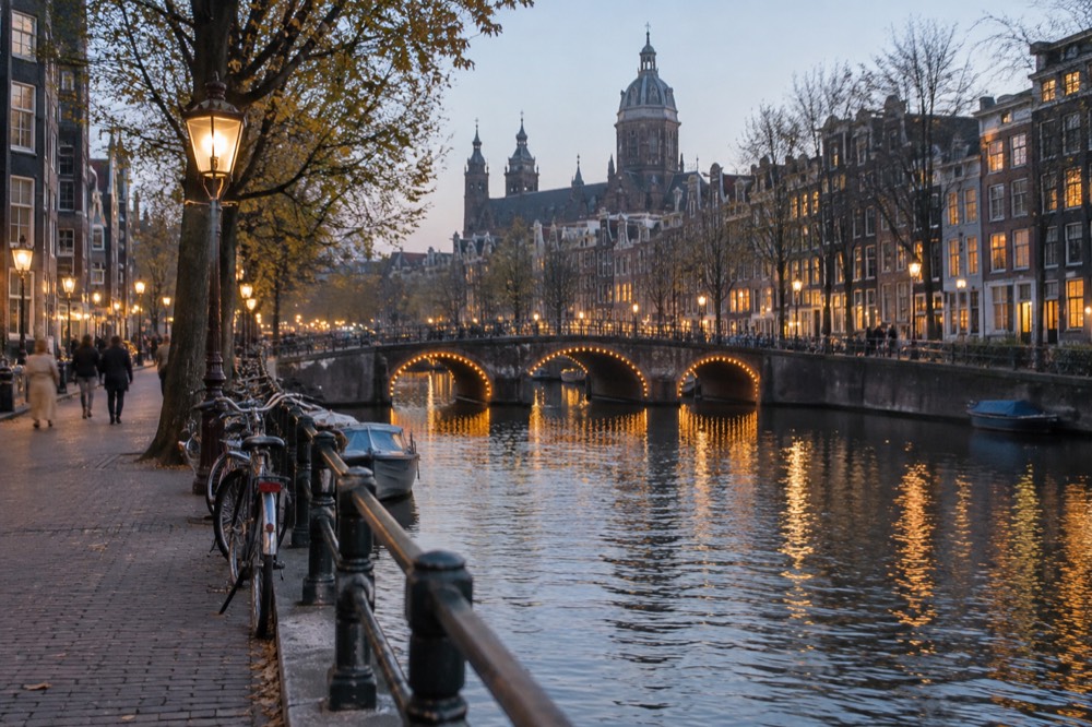 Evening canal in central Amsterdam with illuminated bridges and narrow gabled houses reflected in the water