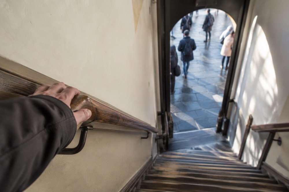 A hand on a wooden handrail partway up a steep Amsterdam staircase