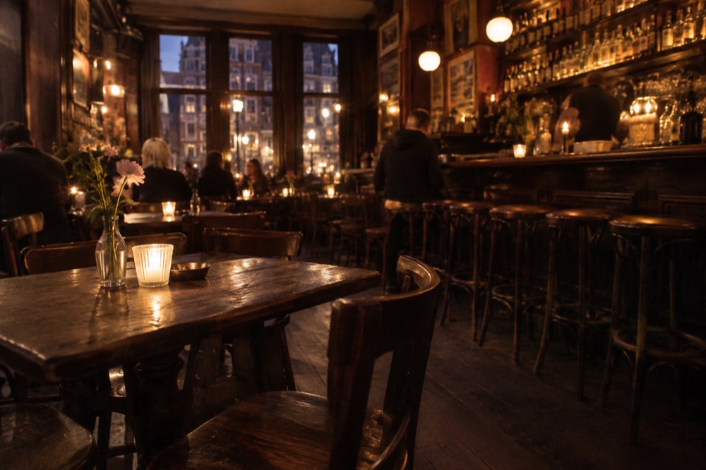A candlelit brown café interior in Amsterdam with wooden tables and a long wooden bar