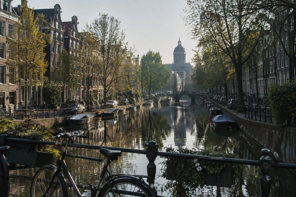 A canal in Amsterdam lined with narrow gabled houses and trees reflected in still water