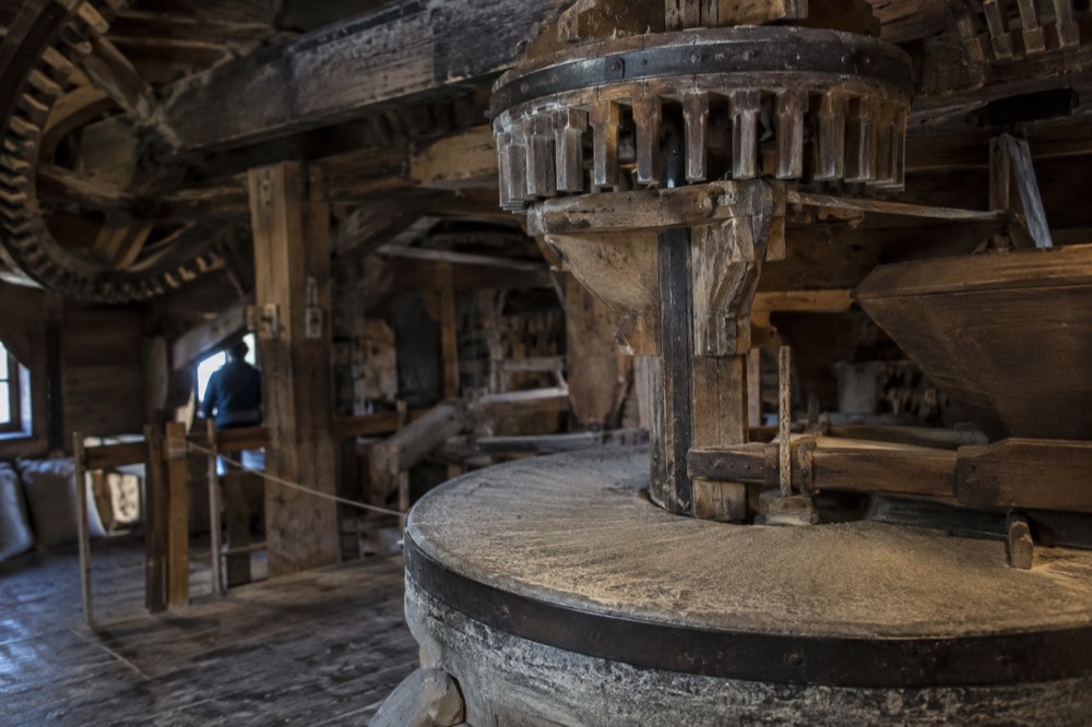 The interior of a working windmill with wooden gears and a millstone in dim light