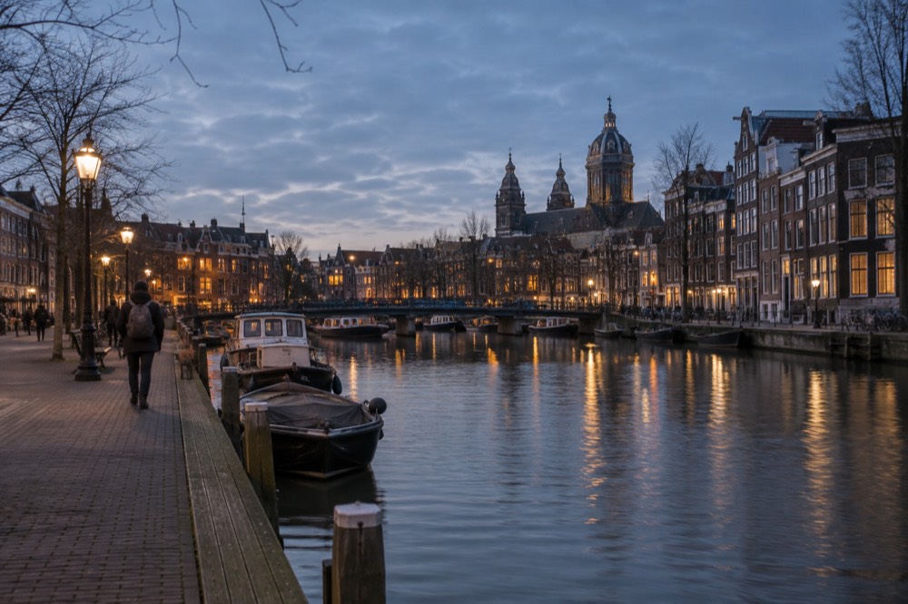A quiet Dutch station platform beside a canal with small boats moored along the bank