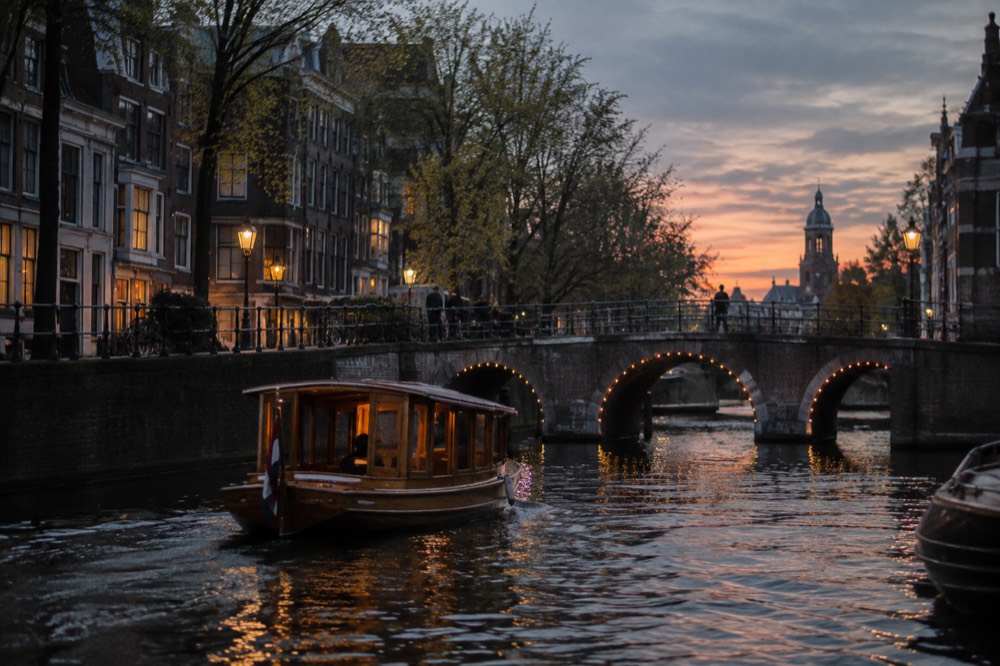 A small wooden saloon boat crossing a canal bridge at sunset