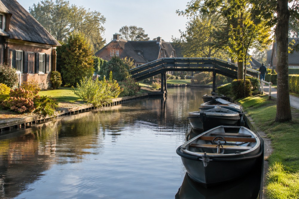 Small electric boats moored along a Giethoorn canal beside a wooden bridge