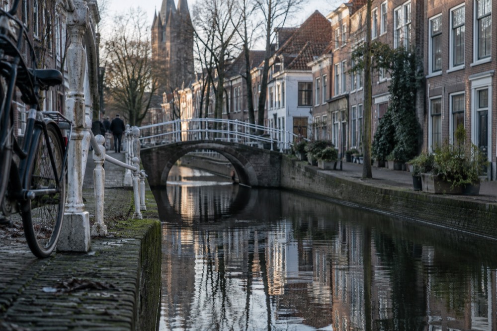 A quiet canal in Delft with old brick houses and a small footbridge