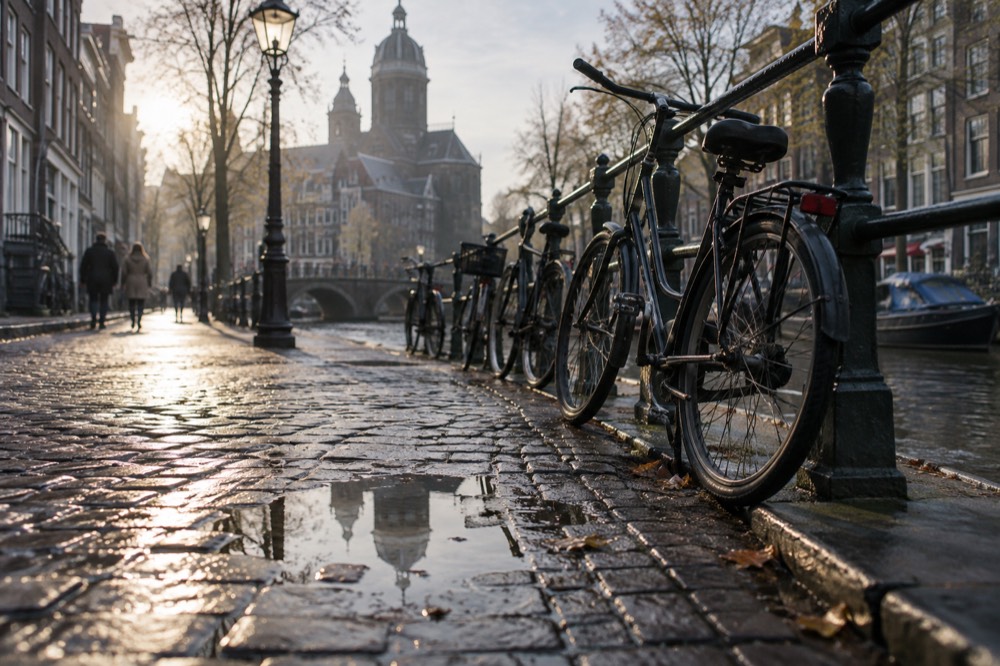 Wet cobblestone street along an Amsterdam canal with bicycles parked against a railing