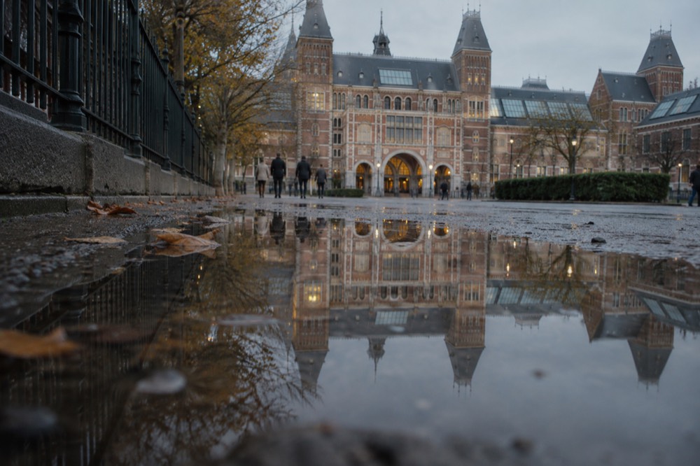 The evening facade of the Rijksmuseum reflected in a quiet street puddle