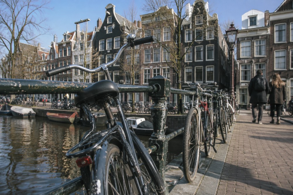 Row of narrow gabled canal houses along a quiet Amsterdam canal with bicycles on a bridge
