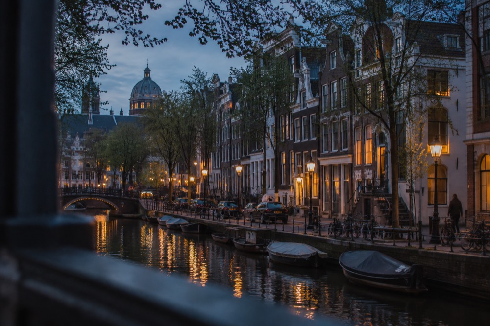 Row of narrow gabled canal houses along an Amsterdam gracht with trees